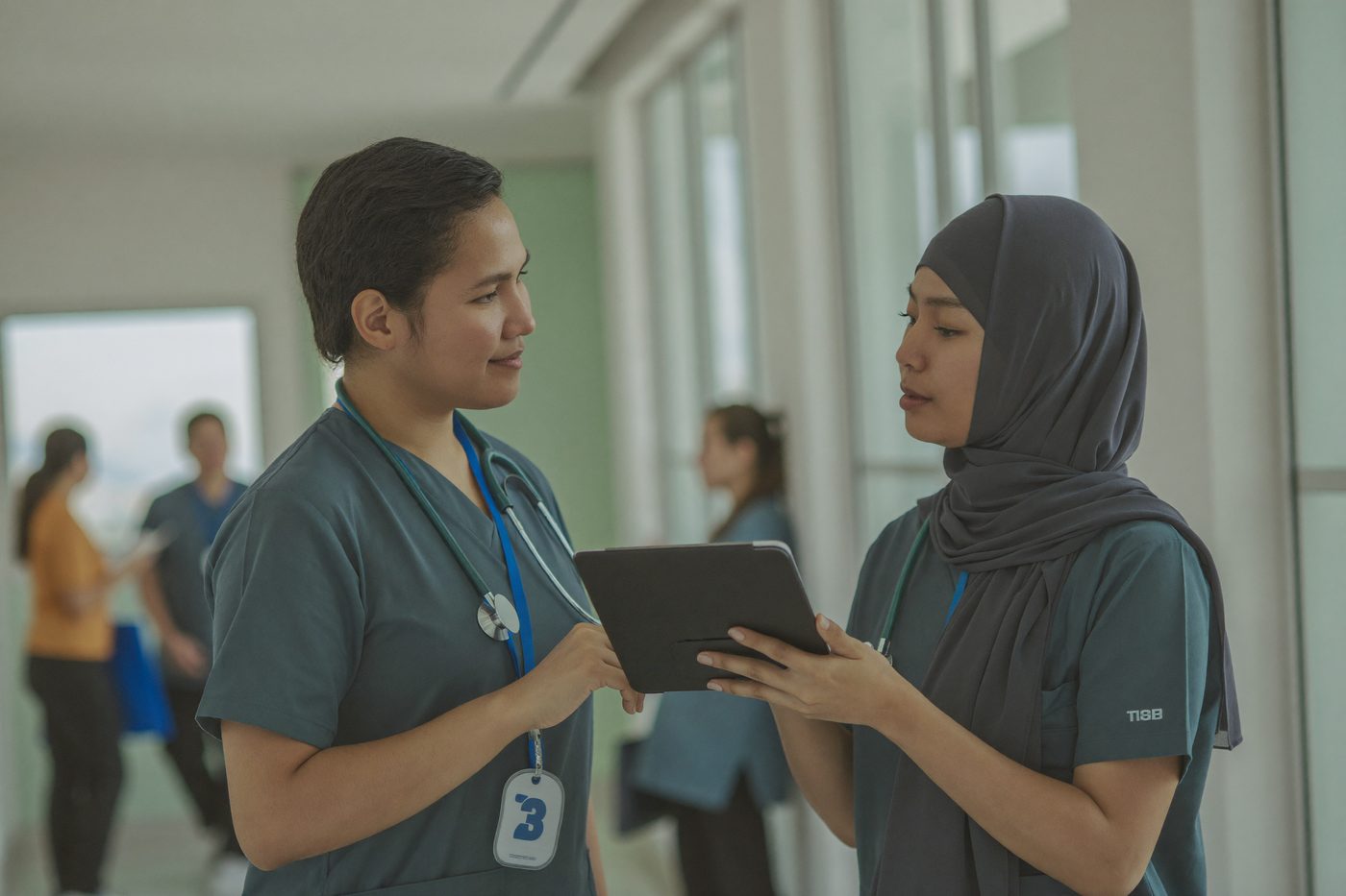 Dua klinisi menelaah data pasien dari tablet saat serah terima sif